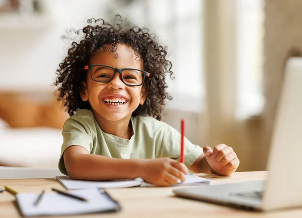 Sonriente afroamericano niño escolar estudiando en línea en el ordenador portátil en casa — Foto de Stock