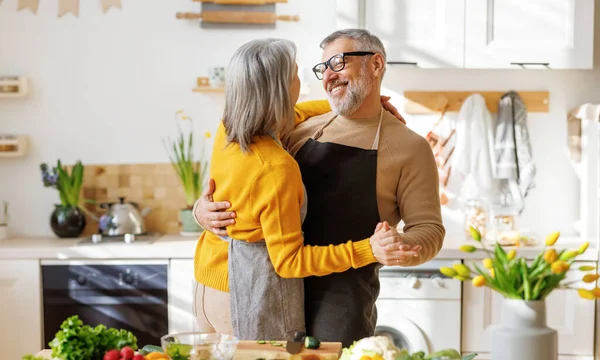 Happy senior elderly couple husband and wife embracing and dancing while cooking together in kitchen — Stock Photo, Image