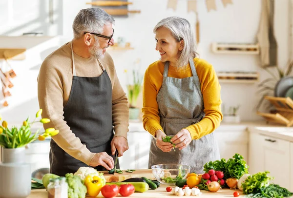 Feliz casal idoso preparar jantar vegetariano juntos, cortar legumes frescos coloridos — Fotografia de Stock
