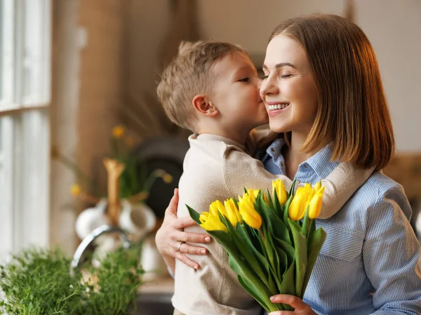 Młoda kobieta matka z kwiat bukiet obejmujący syn podczas otrzymywać gratulacje na dzień matki — Zdjęcie stockowe