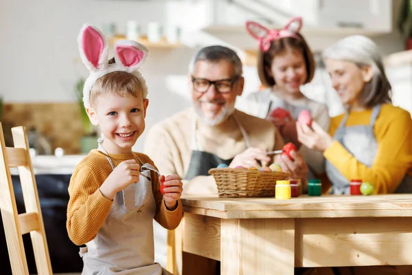 Щасливі маленькі діти створюють красиві розписані яйця на Великдень з люблячими старшими дідусем і бабусею — стокове фото