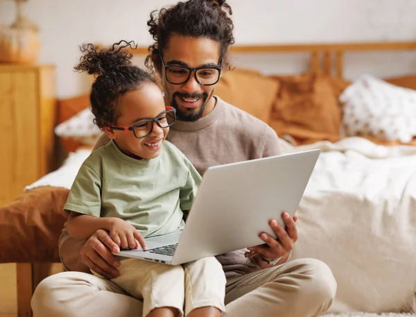 Lykkelig afroamerikansk familiesønn med far som ser morsomme videoer på laptop sammen hjemme – stockfoto