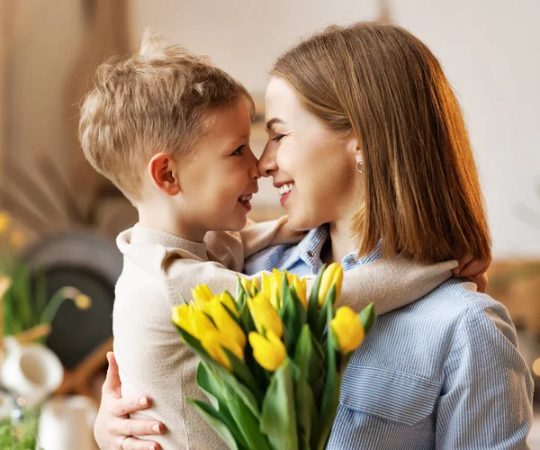 Ung kvinna mor med blomma bukett omfamnande son samtidigt få grattis på mors dag — Stockfoto