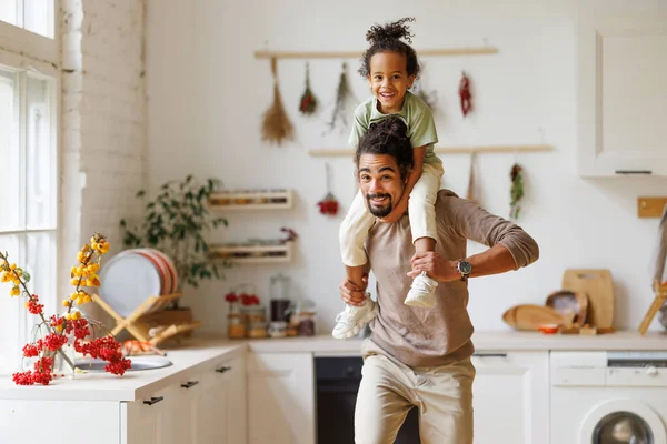Cute little african american child son sitting on father shoulders while playing together at home — Stock Photo, Image