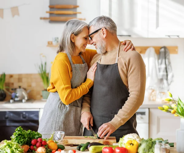 Família idosa feliz casal esposa e marido abraçando enquanto cozinha comida vegetariana juntos — Fotografia de Stock