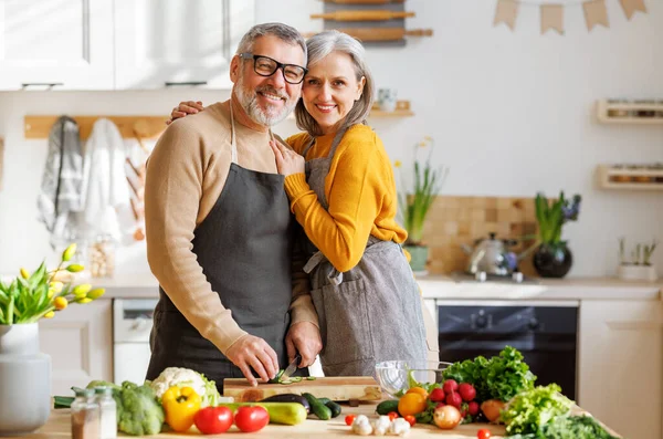 Happy elderly family couple wife and husband embracing while cooking vegetarian food together — Stock Photo, Image