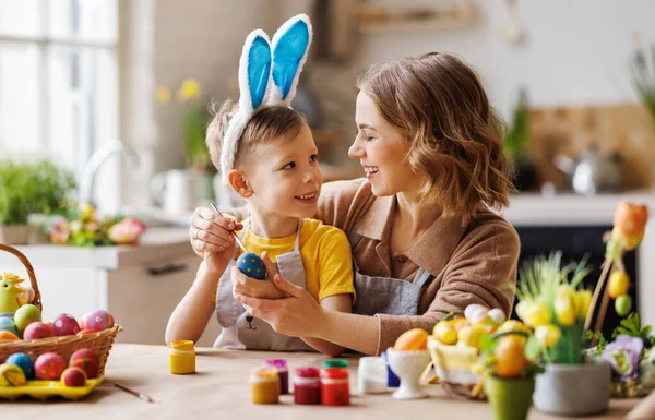Amare la giovane madre insegnando felice figlio bambino a decorare le uova di Pasqua mentre seduto in cucina — Foto Stock