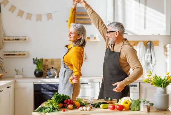 Glückliche Senioren Ehepaar Mann und Frau umarmen und tanzen beim gemeinsamen Kochen in der Küche — Stockfoto