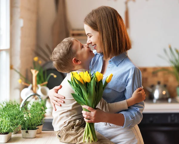 Giovane madre donna con mazzo di fiori che abbraccia il figlio mentre ottiene congratulazioni per la festa della mamma — Foto Stock