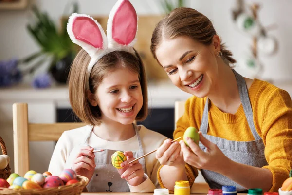 Amar a jovem mãe ensinando a filha criança feliz para decorar ovos de Páscoa enquanto está sentado na cozinha — Fotografia de Stock