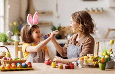 Neşeli mutlu bir aile annesi ve kızı Paskalya yumurtalarını süslerken eğleniyor ve oynaşıyorlar.