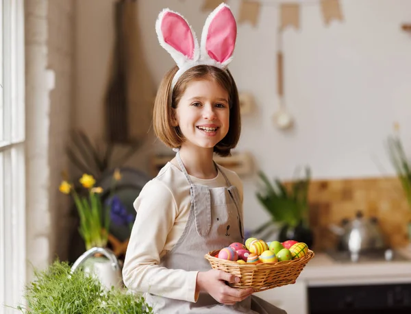 Linda niña feliz con orejas de conejo de felpa celebración cesta de Pascua en la cocina — Foto de Stock