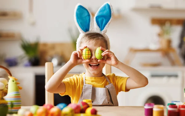 Divertido niño feliz con orejas de conejo de felpa en la cabeza que cubre los ojos con huevos de Pascua multicolores — Foto de Stock