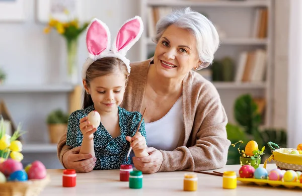 Amare nonna insegnare felice bambina a decorare le uova di Pasqua mentre seduto in cucina — Foto Stock