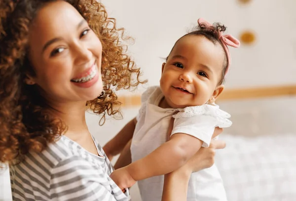 Happy, cheerful ethnic mom holds a laughing baby daughter in her arms. — Stock Photo, Image