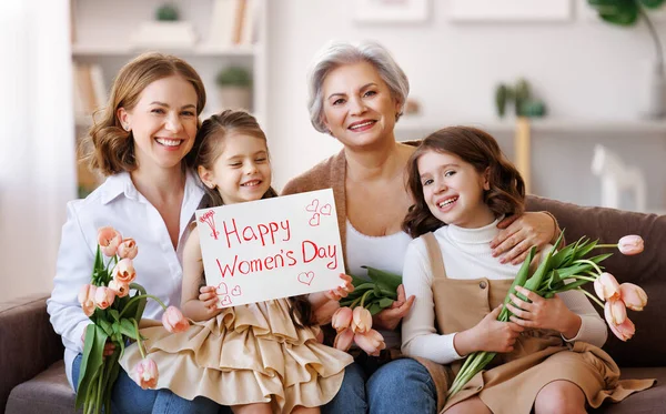 Feliz Día Internacional de la Mujer. familia abuela, madre e hija con flores y un cartel celebran la fiesta —  Fotos de Stock