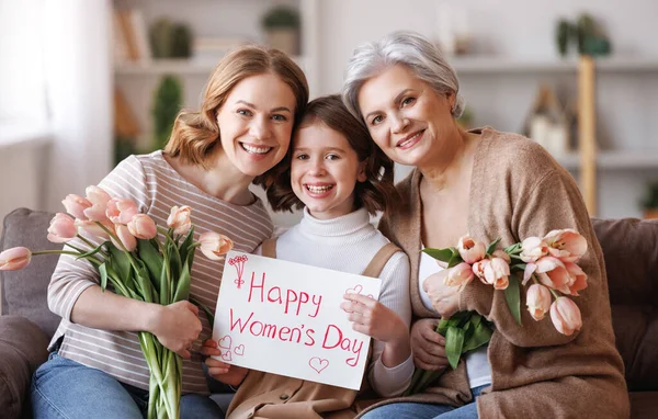 Feliz Dia Internacional da Mulher. avó de família, mãe e filha com flores e um cartaz celebram férias — Fotografia de Stock