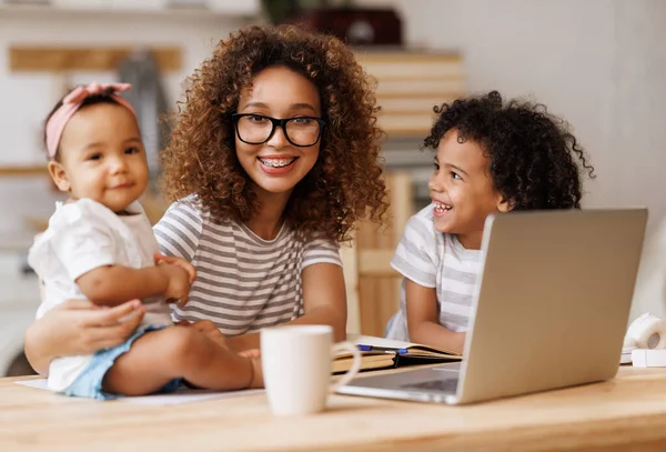 Jovem mulher americana africana feliz freelancer trabalhando remotamente de casa com duas crianças pequenas — Fotografia de Stock