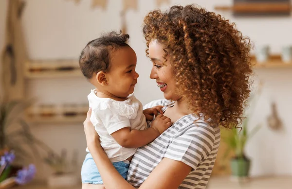 Happy, cheerful ethnic mom holds a laughing baby daughter in her arms. — Stock Photo, Image