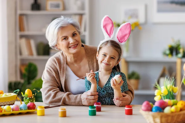 Amare nonna insegnare felice bambina a decorare le uova di Pasqua mentre seduto in cucina — Foto Stock