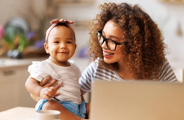 Freelance et maternité. Heureuse jeune femme afro-américaine travaillant à distance avec bébé fille mignonne — Photo