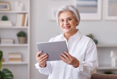 Evde tablet kullanan gülümseyen olgun bir kadın.