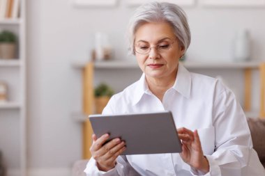 Evde tablet kullanan olgun bir kadın.