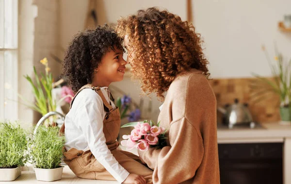 Young ethnic woman mother with flower bouquet embracing son while getting congratulations on Mothers day — Stock Photo, Image