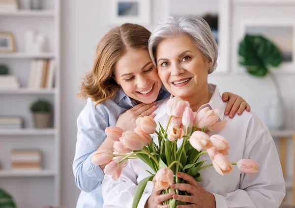Задоволена молода жінка вітає маму з букетом свіжих тюльпанів — стокове фото