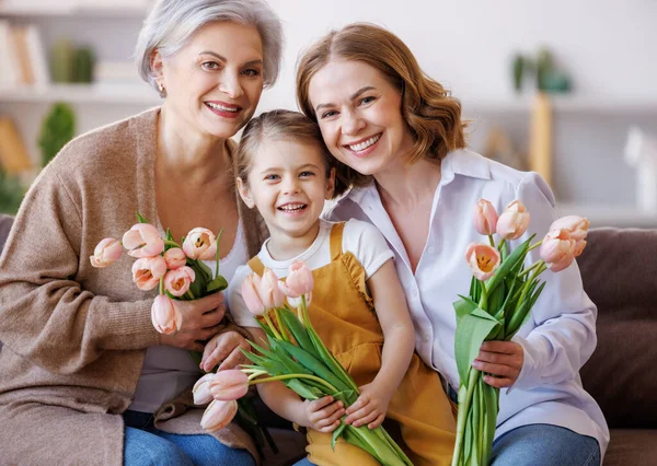 Feliz Día Internacional de la Mujer. la abuela, la madre y la hija con flores celebran alegremente la fiesta el Día de las Madres —  Fotos de Stock