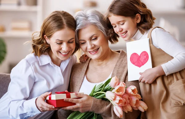 Joyeuse Journée internationale de la femme. fille et petite-fille donnant des fleurs à grand-mère célèbrent la fête des mères à la maison — Photo