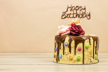 Çikolata parçalarıyla süslenmiş doğum günü pastası ve ahşap masada saklanmış fındık ve gül çiçekleri.
