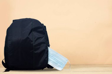 COVID-19 önleme, okula dönüş ve yeni normal konsept. Okul çantasının içinde okul malzemeleri ve ahşap maske var.