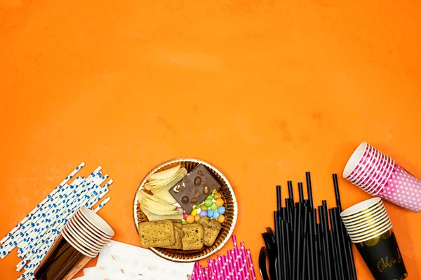 happy birthday concept, Chocolate Candy and straw and chips potato, cookies and disposable cups with plastic forks and paper plate on orange background