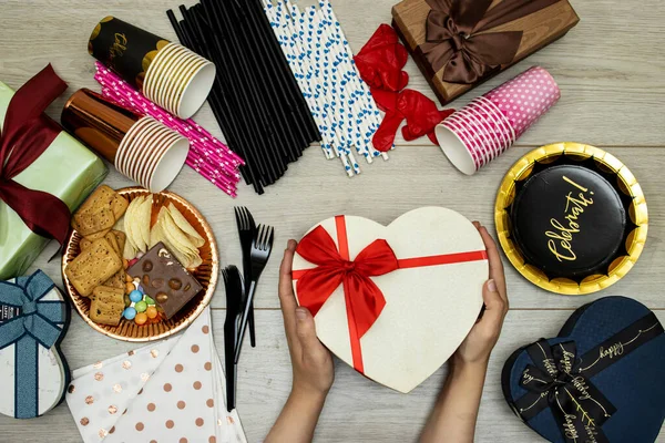 happy birthday concept, Chocolate Candy and straw and chips potato, cookies and disposable cups with plastic forks and gift boxes and plate paper and hands holding heart gift on wood