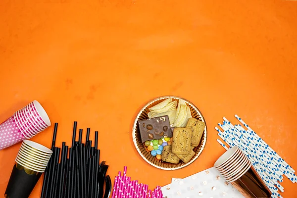 happy birthday concept, Chocolate Candy and straw and chips potato, cookies and disposable cups with plastic forks and paper plate on orange background