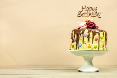 Çikolata parçalarıyla süslenmiş doğum günü pastası ve ahşap masada saklanmış fındık ve gül çiçekleri.