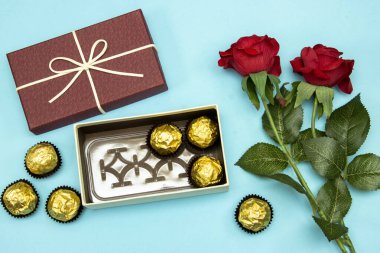Hediye ya da hediye olarak altın değerindeki çikolatalı şekerlemeler mavi arka planda kırmızı güller, mutlu sevgililer günü konsepti