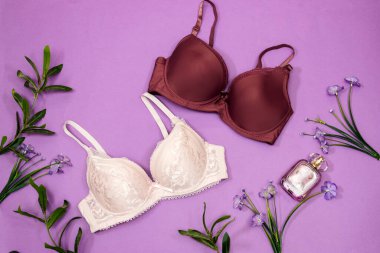  Zarif dantel sutyen, parfüm şişesi ve mor arka planda çiçekler. Şık iç çamaşırları düz yatıyordu.