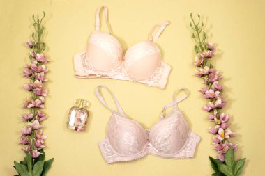 Sarı arka planda parfüm şişesi ve çiçekli zarif dantelli sutyen. Şık iç çamaşırları düz yatıyordu.