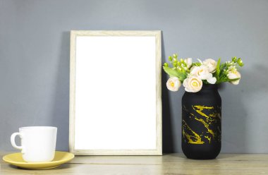 Hayat: boş çerçeve maketi, çiçek vazosu ve ahşap masa üzerinde bir fincan kahve. Zarif çalışma alanı, ev ofisi konsepti