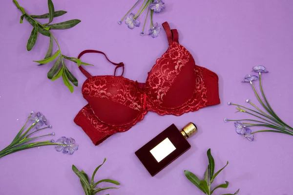 Zarif dantel sutyen, parfüm şişesi ve mor arka planda çiçekler. Şık iç çamaşırları düz yatıyordu.