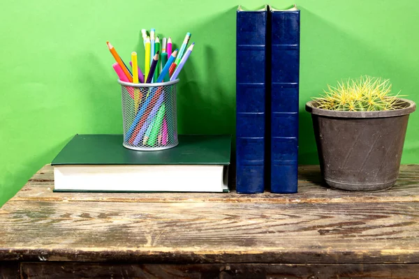 Echinocactus Cactus Potted  with  books and pencils case on wood table over green background