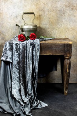 Eski ahşap masanın üzerinde gri tekstil ve Arap çaydanlığı olan güzel kırmızı güllerin klasik fotoğrafı.