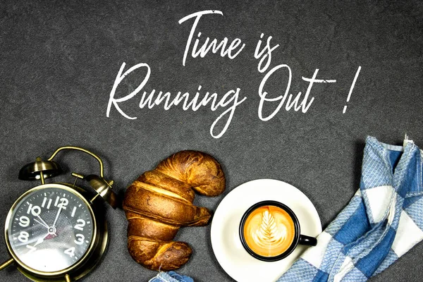 Time is Running Out Concept, Fresh baked croissants on black board for breakfast and coffee cup with leaf late art and alarm clock showing seven o\'clock on gray grunge background