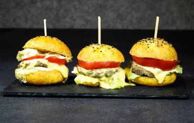 three homemade  burger with cheese and meat, tomato and salad in blackboard plate
