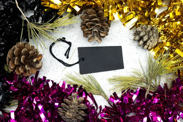 black and golden Tinsel with pine cones around a black empty tag. merry Christmas concept