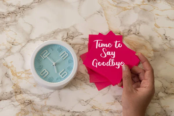 woman holding a pink card with time to say goodbye text with alarm clock