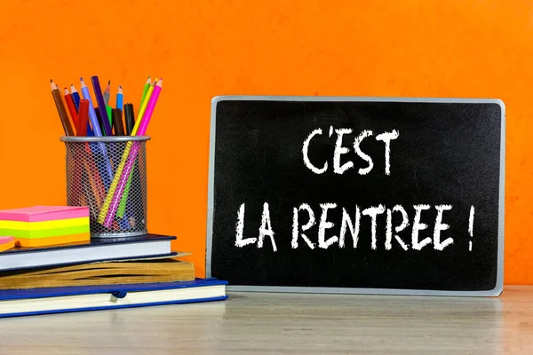 Back to school concept - blackboard with french word : c'est la rentre with pencil-box and books, notebook and sticky note on wooden table