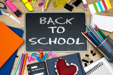 Back to school concept - blackboard with pencil-box and books, notebooks and sticky note and calculator with pins, felt pen and heart shape on wooden table